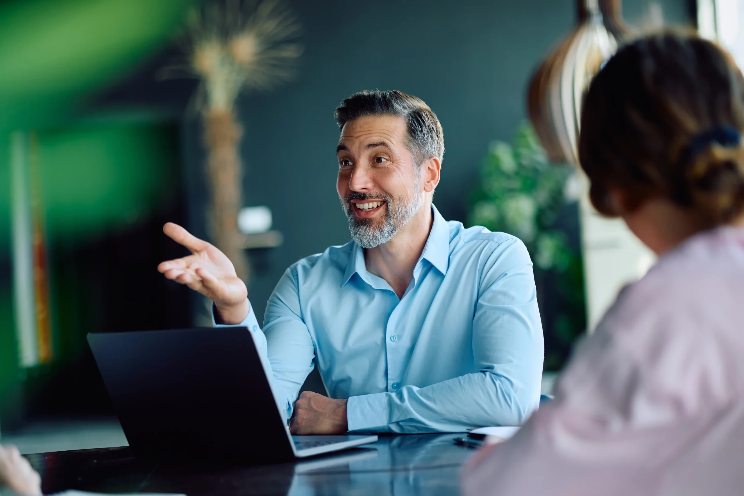 A consultant gesturing while talking with a colleague across a laptop.